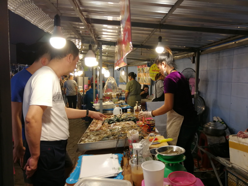 People shopping at a street food market stall with seafood under lights at Chiang Mai Night Market Food Guide.
