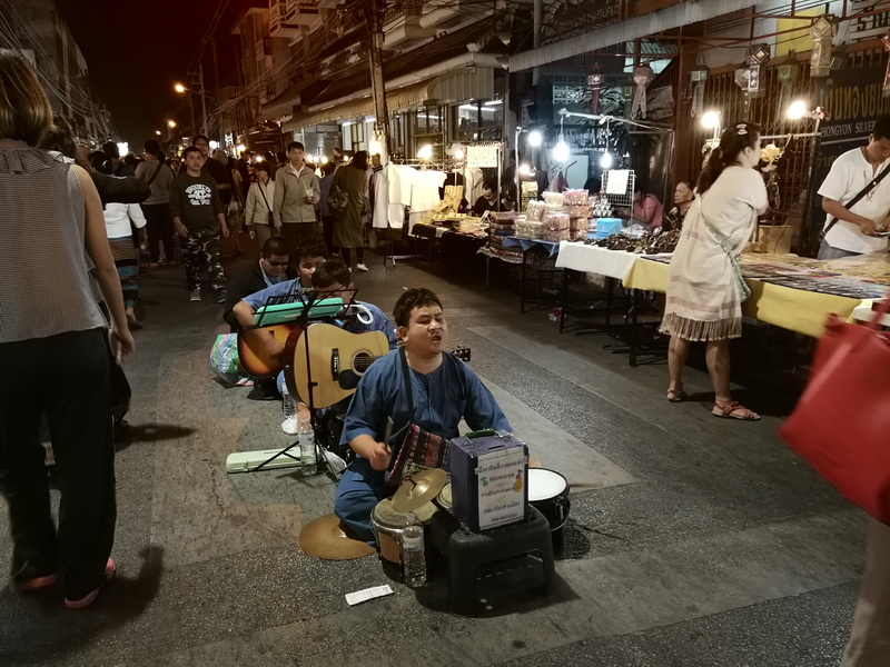 Street performers playing music at night with market stalls and crowd in background at Saturday Walking Street Chiang Mai.