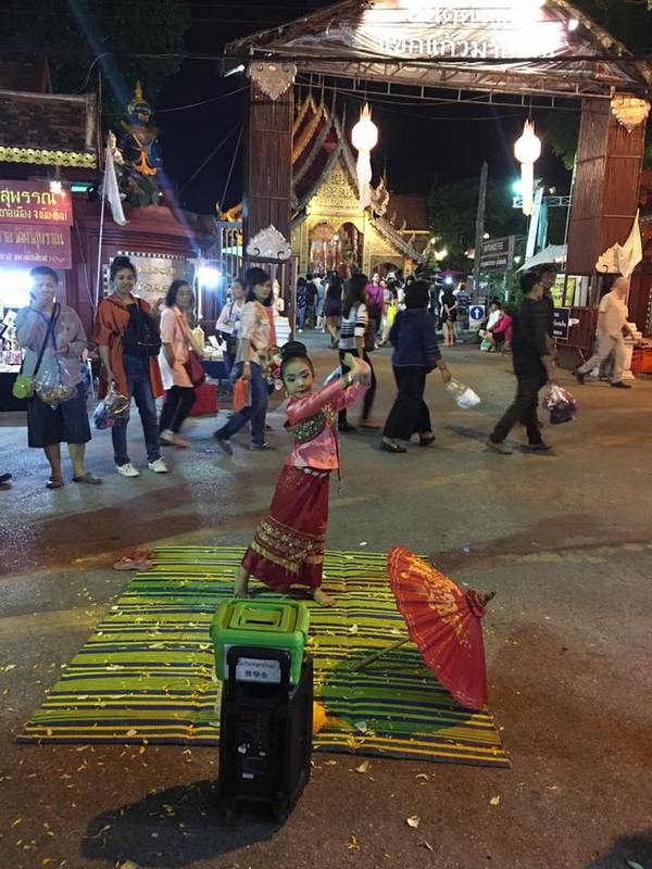 Night Cultural Performance Scene at Wua Lai Walking Street Chiang Mai Girl performing traditional dance on bamboo mat with umbrella at night near temple at Wua Lai Walking Street Chiang Mai.
