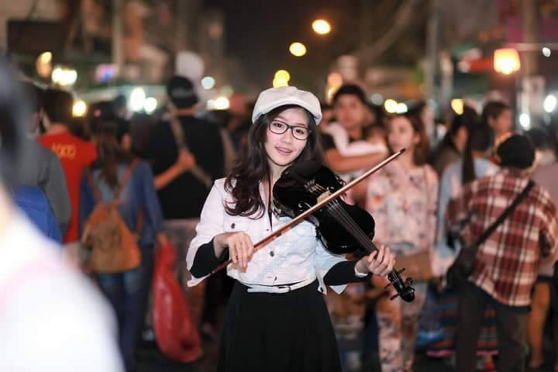 Music Night Performance at Sun Day Walking Street Chiang Mai Woman playing violin amidst crowd at night with colorful lights behind her at Sun Day Walking Street Chiang Mai.