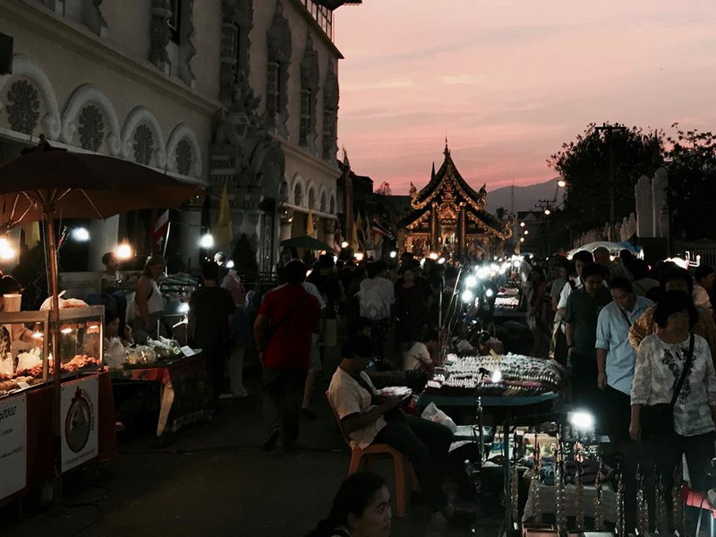 Night Market at Dusk in Chiang Mai at Sunday Night Market Chiang Mai Crowded street market at sunset with jewelry stalls and a traditional Thai pavilion in the background at Sunday Night Market Chiang Mai.