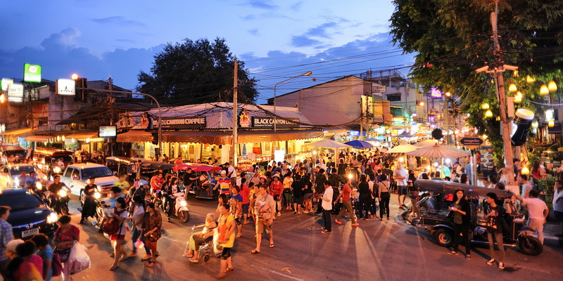 Bustling Night Market Scene at Sunday Night Market Chiang Mai Vibrant street scene with crowds, shops, and motorcycles at dusk at Sunday Night Market Chiang Mai.