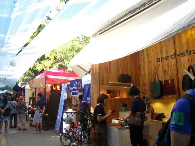 People shopping at outdoor market with colorful umbrellas and stalls at Nimmanhaemin road.