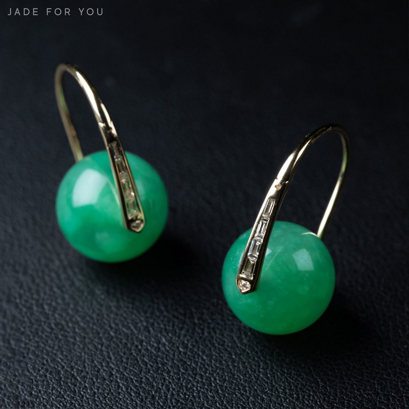Green gemstone earrings with gold hooks on a black textured surface at Chiang Mai Jade Factory.
