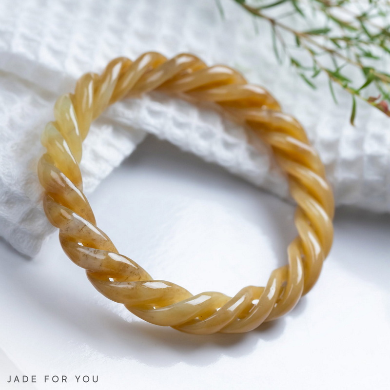 Amber twisted bracelet on white textured surface with green leaves nearby at Chiang Mai Jade Factory.