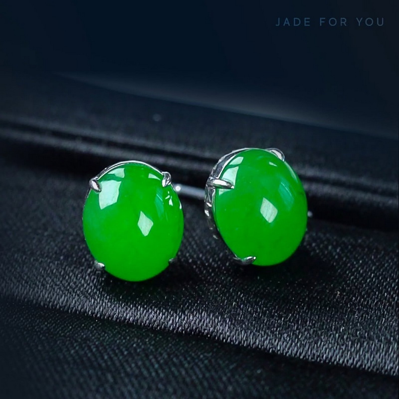 Pair of green jade earrings with silver settings on black fabric background at Orchid Jade Factory.