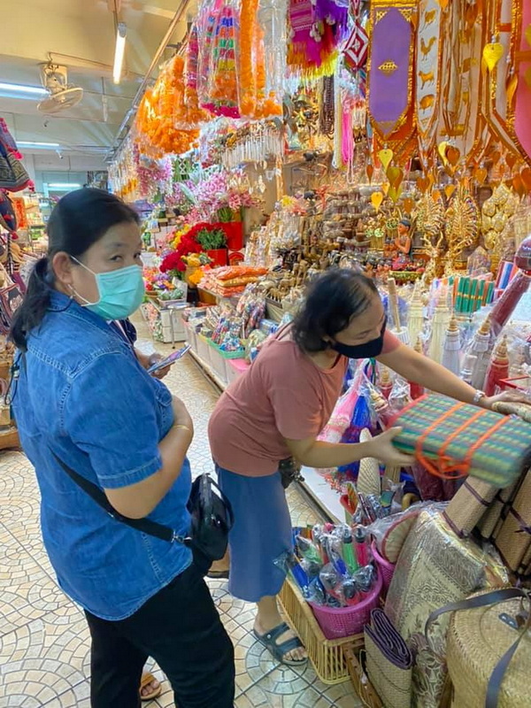 Shopping at a Market Stall in Chiang Mai at Best Street Food Markets In Chiang Mai Two women shopping for colorful decorations and textiles in a busy market stall at Best Street Food Markets In Chiang Mai.