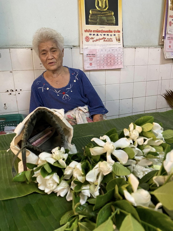 Elderly Woman with Flowers at Best Street Food Markets In Chiang Mai Elderly woman sitting behind a table with white flowers and green leaves in front of her at Best Street Food Markets In Chiang Mai.