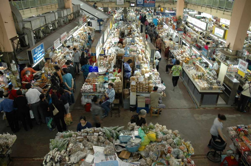 Indoor market with busy stalls and shoppers browsing goods at Warorot Market.
