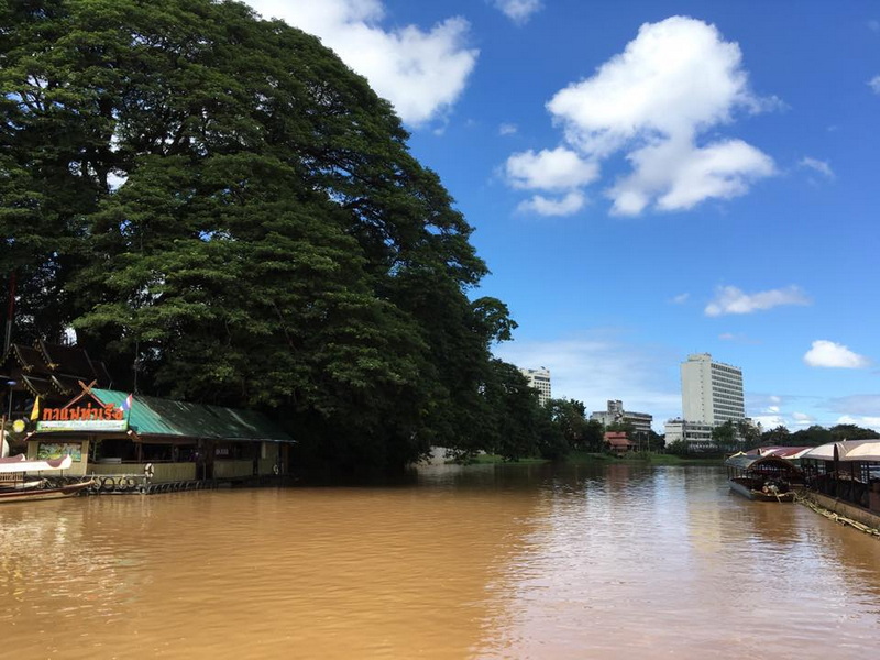 River with greenery and city buildings under blue sky with clouds at Chiang Mai Cruise To Wiang Kum Kam.