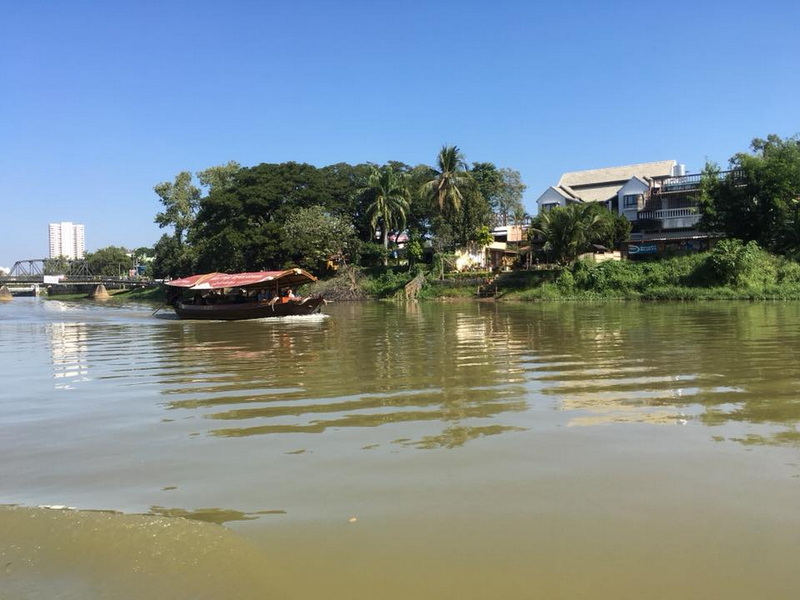 Scenic River Scene at Chiang Mai Cruise To Wiang Kum Kam A boat moving on a river with lush greenery and buildings nearby at Chiang Mai Cruise To Wiang Kum Kam.