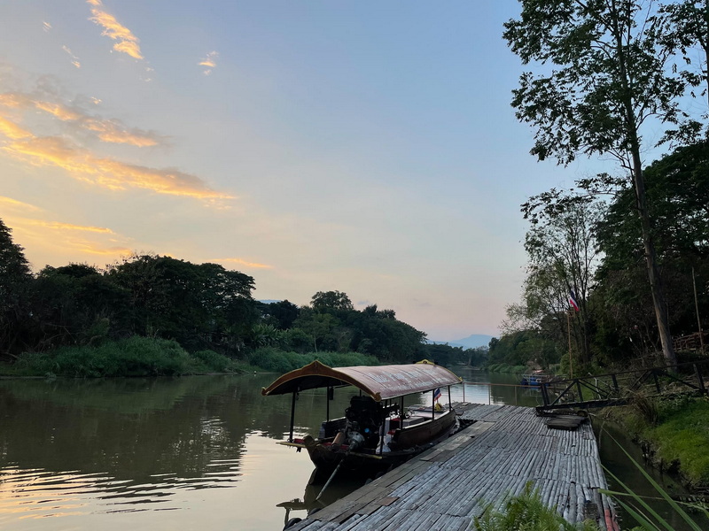 Boat with a curved roof docked on a quiet river surrounded by greenery and trees at Chiang Mai Cruise To Wiang Kum Kam.