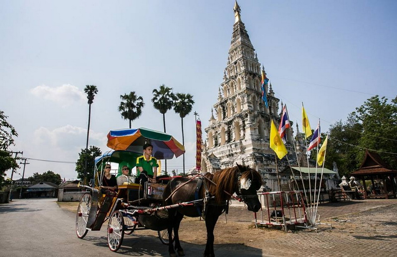 Horse-drawn carriage in front of a white temple with flags and palm trees nearby at Chiang Mai Cruise To Wiang Kum Kam.