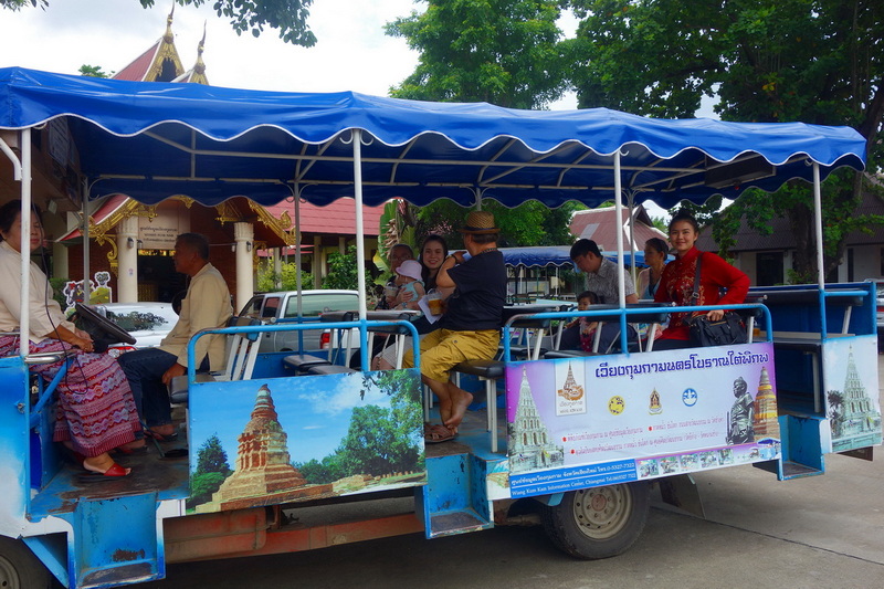 Tour vehicle with passengers in front of a temple among trees at Chiang Mai Cruise To Wiang Kum Kam.