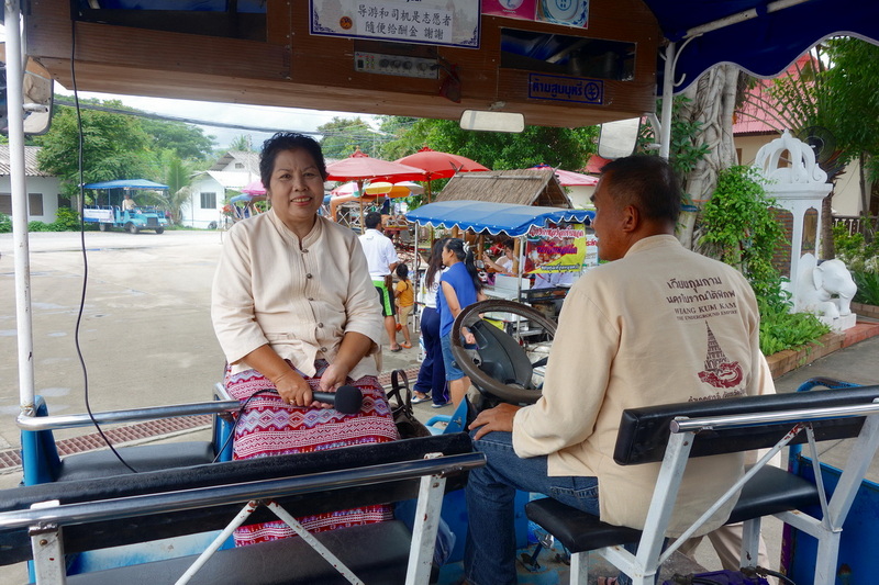 Woman with microphone in boat talking to man at steering wheel during market day at Chiang Mai Cruise To Wiang Kum Kam.