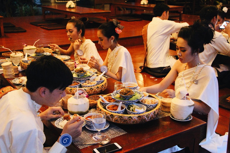 Traditional Dinner Gathering at Khantoke People in traditional clothing enjoying a meal with various dishes on a wooden table at Khantoke.