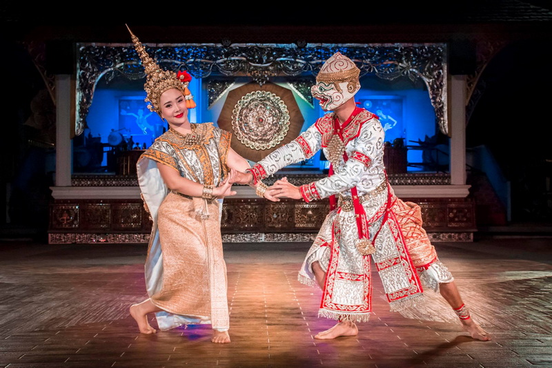 Two dancers in elaborate costumes performing on stage with decorative elements behind them at Khantoke.
