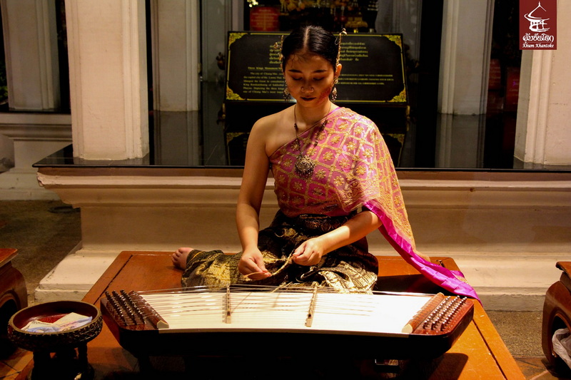 Woman in traditional dress playing a stringed instrument indoors at Khantoke Dinner.