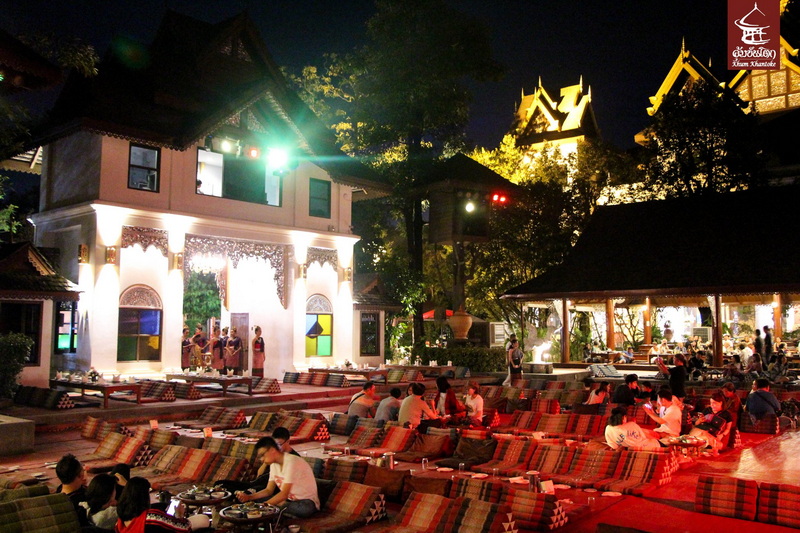 Night Scene of Outdoor Dining at Khum Khantoke Outdoor dining area at night with cushions and traditional-style buildings with colorful lighting at Khum Khantoke.
