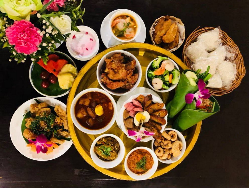 Traditional Thai Food Platter at Khantoke Dinner Assorted Thai dishes and fruits with decorative flowers and sauces on a dark surface at Khantoke Dinner.