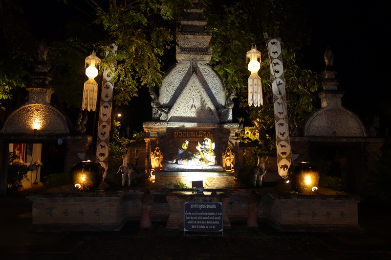Night scene with a lit monument, sculptures, lanterns, and trees surroundings at Khantoke Dinner.