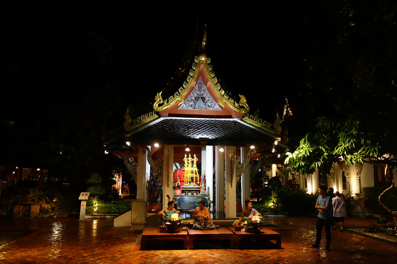 Night view of a decorated pavilion with shrine and seated people in front, illuminated by lights at Khantoke.