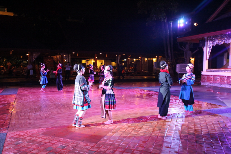 People in traditional costumes performing on stage at night outdoors at Khantoke Dinner.