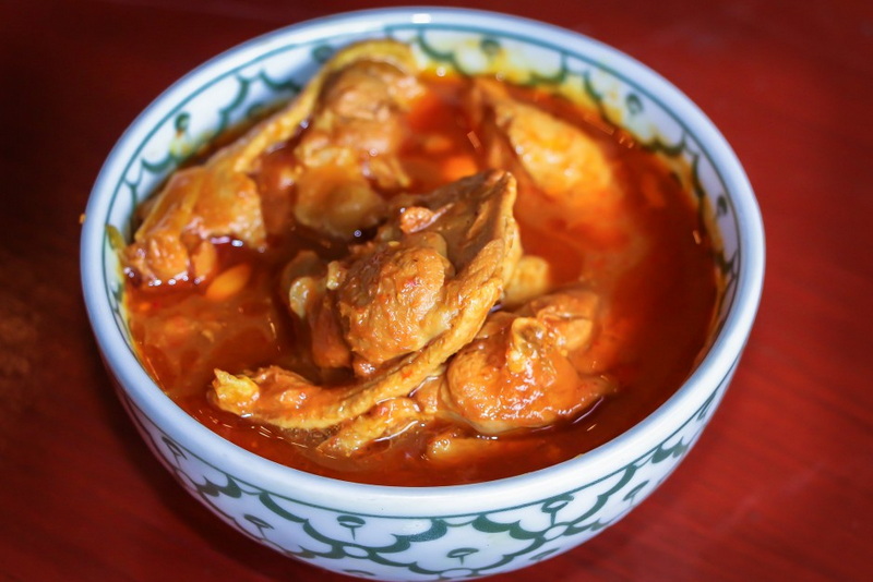 Chicken Stew in a Bowl at Khum Khantoke Bowl of reddish chicken stew with vegetables on a wooden surface at Khum Khantoke.