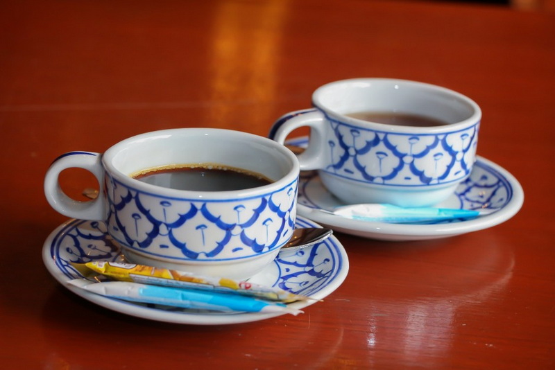 Two cups of black coffee with patterned saucers on a wooden table at Khum Khantoke.