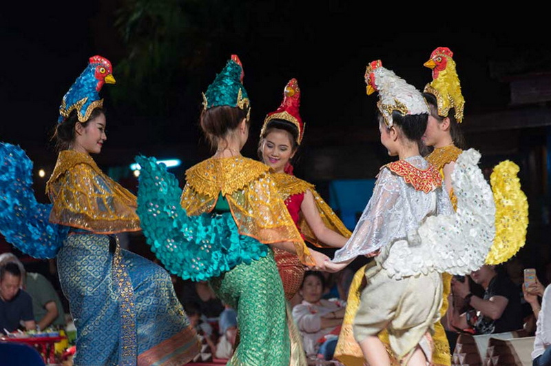 Women in vibrant traditional outfits performing a dance indoors in front of an audience at Old Chiangmai Cultural Center Khantoke.