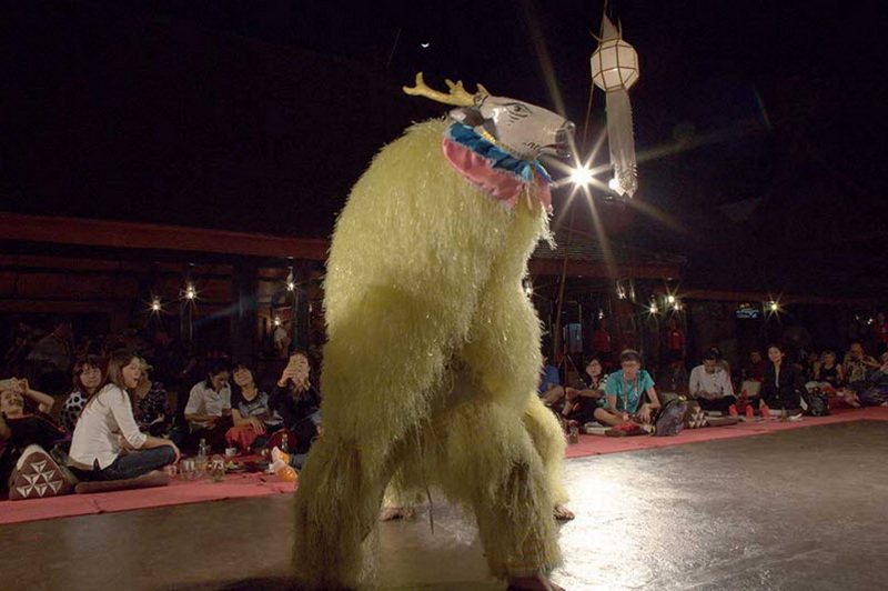 Person in a furry yellow mythical creature costume performing indoors with seated audience nearby at Old Chiangmai Cultural Center.