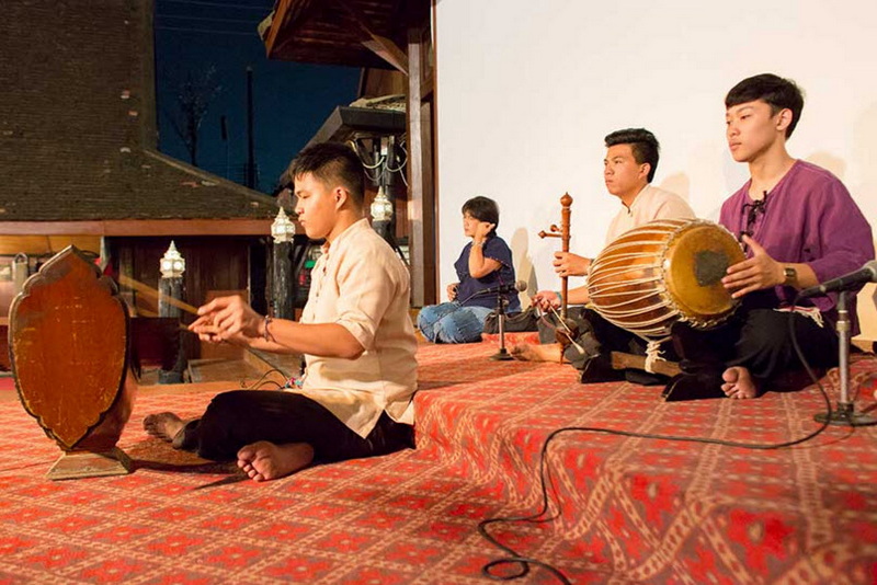 Four boys playing traditional musical instruments on a red patterned carpet indoors at Old Chiangmai Cultural Center Khantoke.