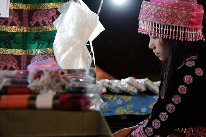 Woman in traditional dress with pink headdress sitting at a market stall at Old Chiangmai Cultural Center Khantoke.