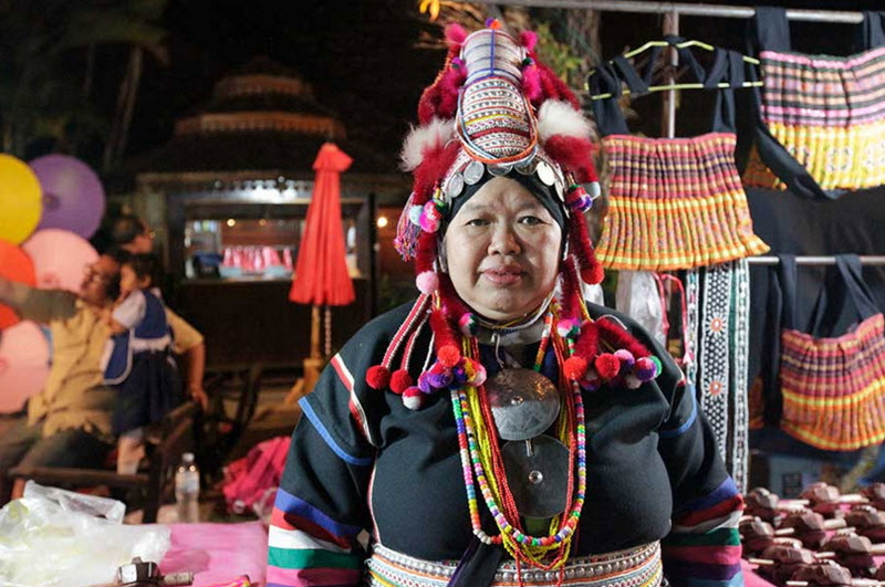 Woman wearing traditional dress and headdress at a market stall with colorful textiles at Khantoke.