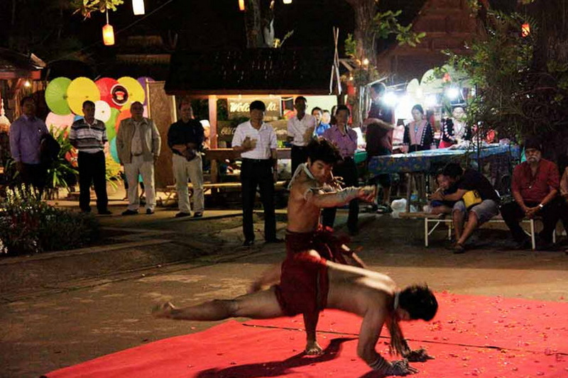 Young performer dances on a red mat during a night cultural event with lantern decorations at Old Chiangmai Cultural Center Khantoke.