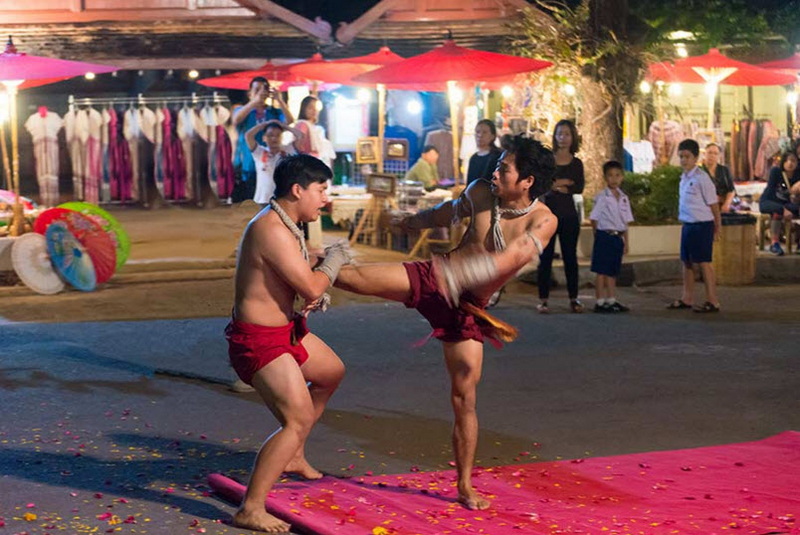 Two performers engaging in martial arts demonstration at night with spectators nearby at Old Chiangmai Cultural Center Khantoke.