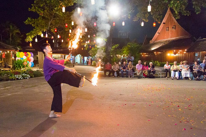 Performer in traditional outfit ignites fire during an outdoor night show with audience watching at Khantoke Dinner.