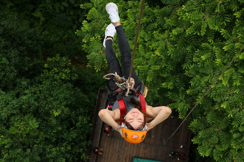 Zip Line Adventure in Jungle at Jungle Flight Zipline Chiang Mai Girl with helmet and harness zip lining through lush green forest canopy at Jungle Flight Zipline Chiang Mai.