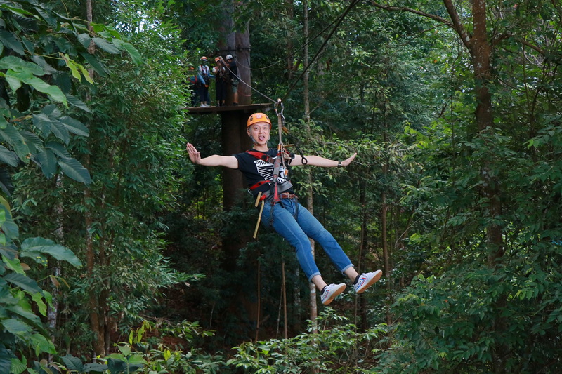 Forest Zip Line Adventure at Jungle Flight Zipline Chiang Mai Woman gliding on a zip line through lush green forest canopy with safety gear on at Jungle Flight Zipline Chiang Mai.