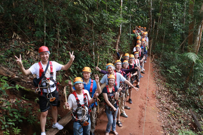 Group of people with helmets and harnesses walking on forest trail surrounded by trees at Zipline Adventure Chiang Mai.