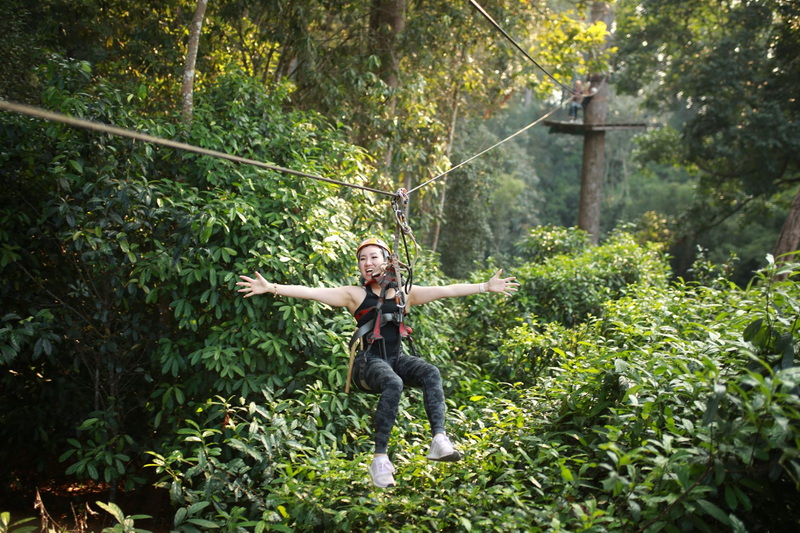 Woman enjoying ziplining through lush jungle canopy with safety gear at Jungle Flight Zipline Chiang Mai.