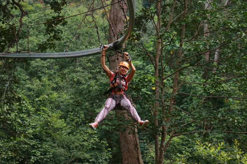 Woman smiling on zipline in lush green forest with helmet and harness at Jungle Flight Zipline Chiang Mai.