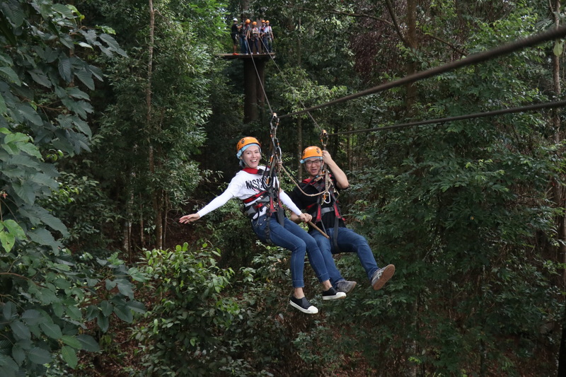 Jungle Zip Line Adventure at Jungle Flight Chiang Mai Two people zip lining through lush jungle with helmets and harnesses on at Jungle Flight Chiang Mai.