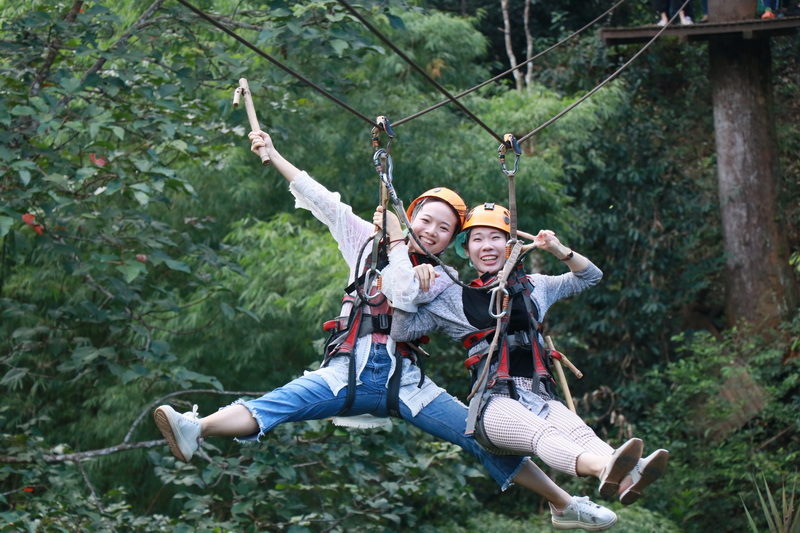 Women on Zip Line Adventure at Jungle Flight Chiang Mai Two women with helmets and harnesses on a zip line through a dense forest at Jungle Flight Chiang Mai.