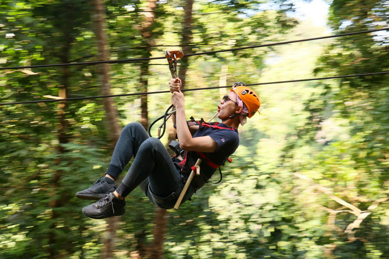 Jungle Ziplining Adventure at Jungle Flight Zipline Chiang Mai Person with helmet and harness ziplining through lush forest canopy at Jungle Flight Zipline Chiang Mai.