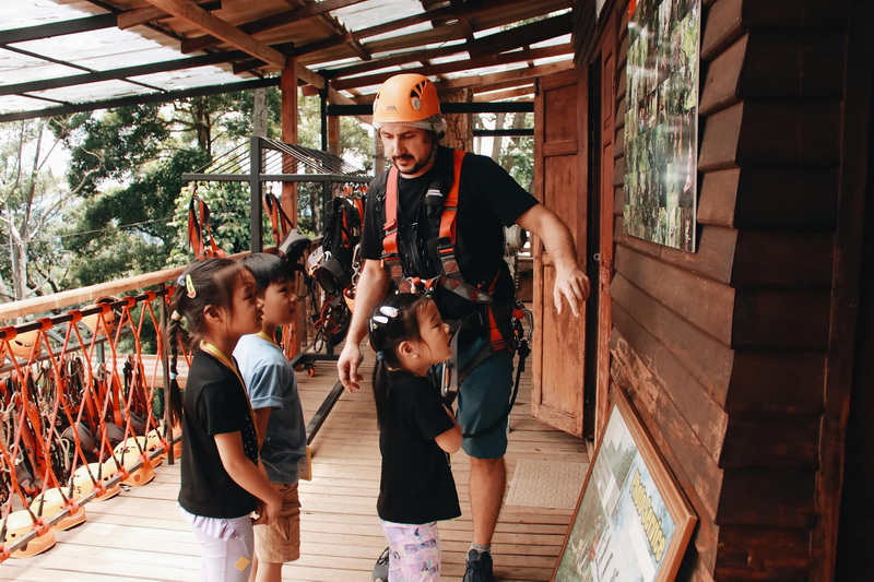 Man explains safety gear to children on balcony at adventure park at Jungle Flight Chiang Mai.