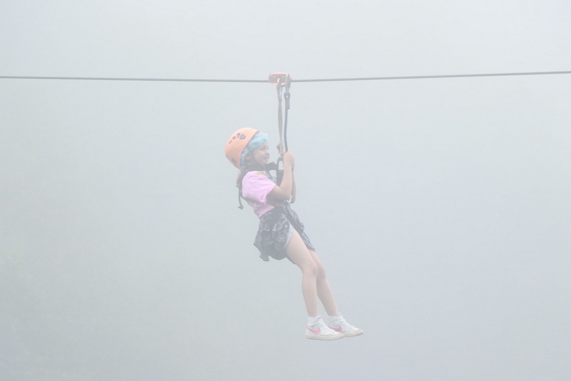 Girl on Zip Line Adventure at Jungle Flight Chiang Mai Girl in helmet and harness riding zip line through foggy landscape at Jungle Flight Chiang Mai.
