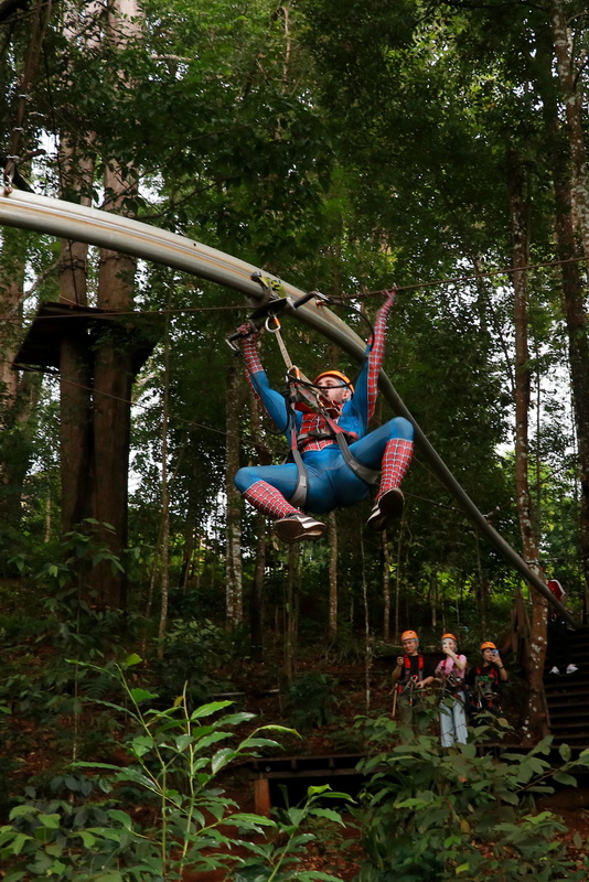 Person dressed as Spider-Man riding a zip line through a wooded area at Jungle Flight Chiang Mai.
