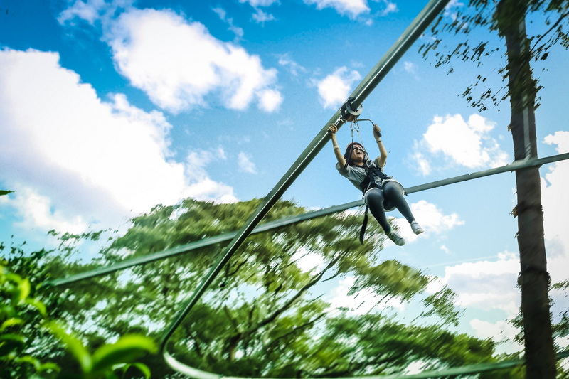 Person gliding on a zipline above dense forest with blue sky and clouds at Jungle Flight Zipline Chiang Mai.