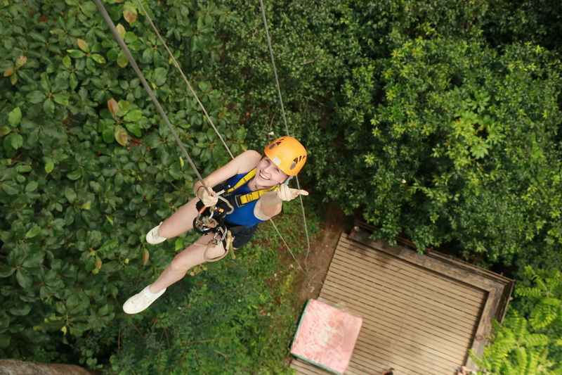 Young woman ziplining through dense green forest during an outdoor adventure at Jungle Flight Chiang Mai.